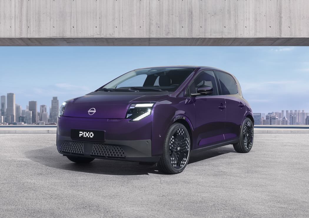 Three-quarter front view of a purple Nissan PIXO electric city car parked beneath a modern concrete structure, with a city skyline in the background.